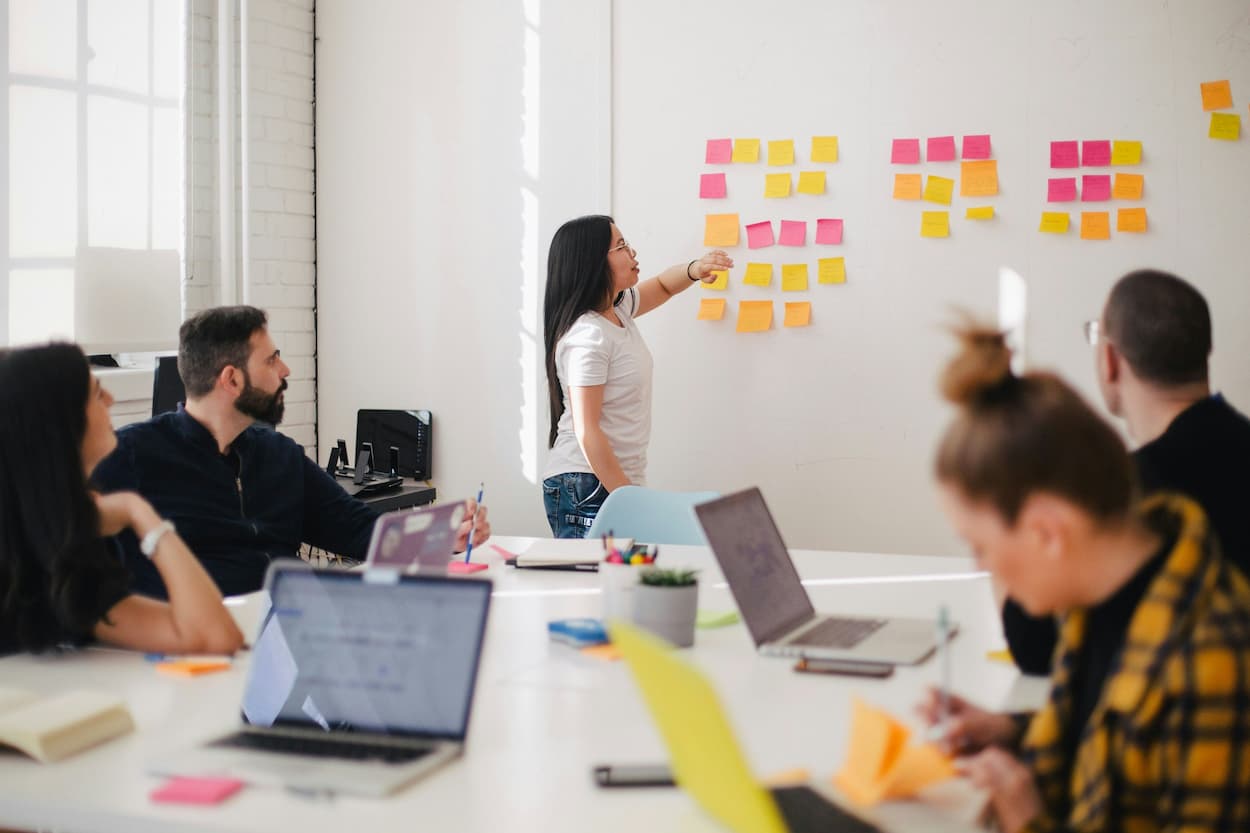 Woman in a meeting with 4 others, sticking notes on a whiteboard